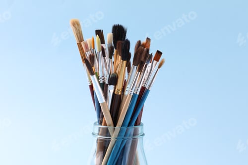 Preview: Set of paintbrushes in glass jar on light blue background, closeup