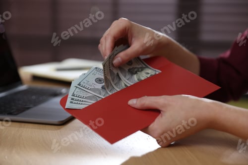 Preview: Woman holding envelope with money at wooden table indoors, closeup