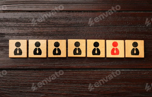 Preview: Dismissal. Cube with red human icon among others with black ones on wooden background, top view