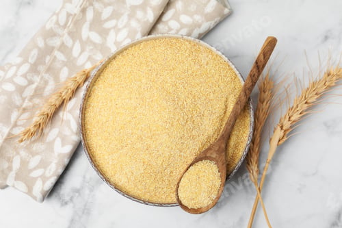 Preview: Raw semolina in bowl with spoon and spikes on white marble table, flat lay