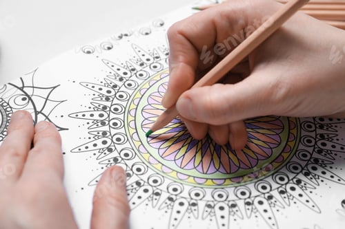 Preview: Woman coloring antistress picture with pencils at white table, closeup