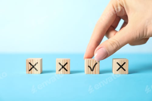 Preview: Woman putting wooden cube with checkmark next to others with cross marks on blue table, closeup. Fol