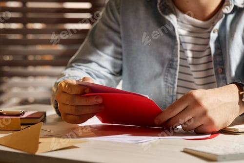 Preview: Man opening envelope with letter at wooden table indoors, closeup