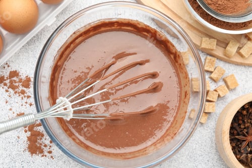 Preview: Chocolate dough with whisk in bowl and spices on grey textured table, flat lay