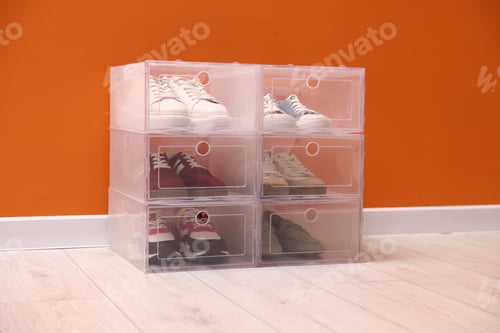 Preview: Different footwear in plastic boxes on floor near orange wall indoors. Shoe storage