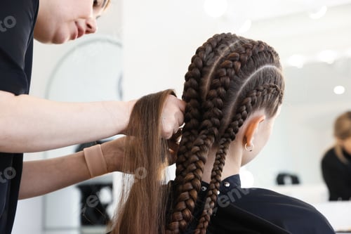 Preview: Hairstylist braiding teenage girl's hair in salon, closeup