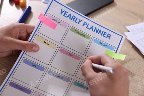 Preview: Man using yearly planner at wooden desk, closeup