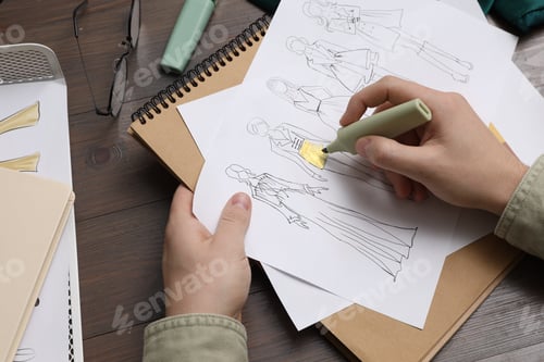 Preview: Fashion designer drawing sketch of outfits at wooden desk, closeup