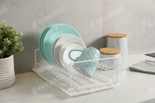 Preview: Drainer with different clean dishware and cup on light table indoors