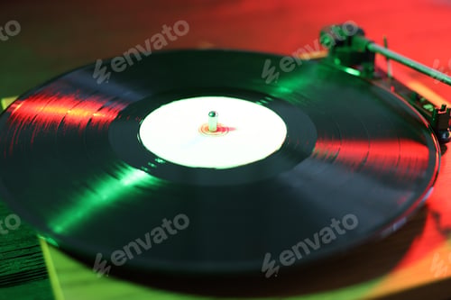Preview: Modern turntable with vinyl record on table in color lights, closeup