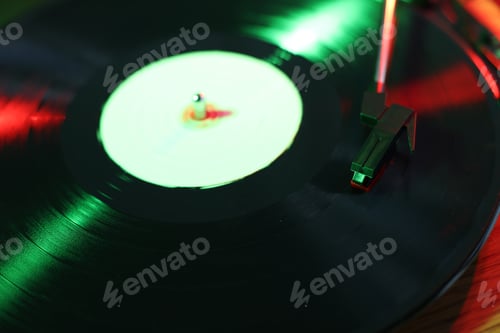 Preview: Modern turntable with vinyl record on table in color lights, closeup