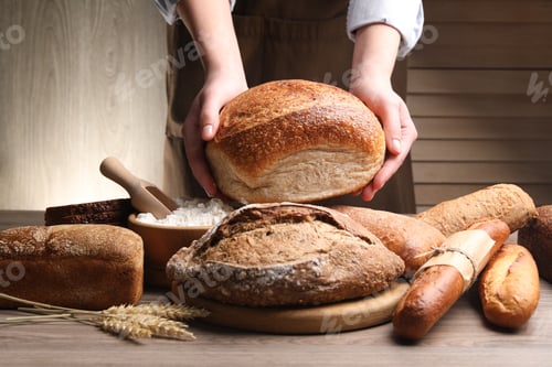 Preview: Woman with different types of bread, flour and spikes at wooden table, closeup