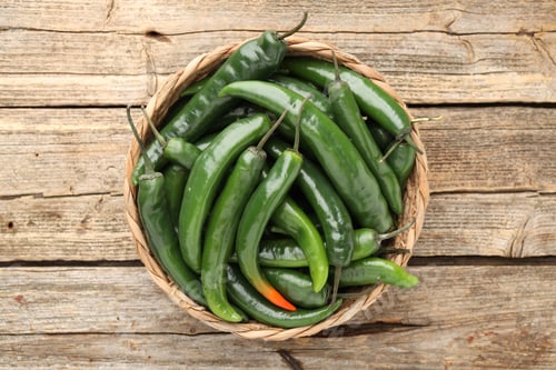 Preview: Fresh chili peppers in wicker basket on wooden table, top view