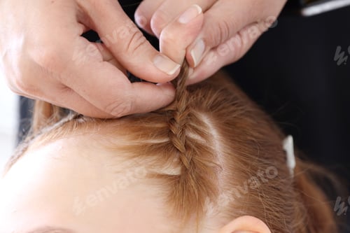 Preview: Hairstylist braiding teenage girl's hair indoors, closeup