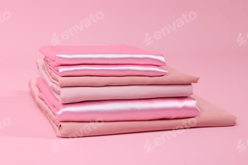 Preview: Stack of fresh bed linens on pink background, closeup