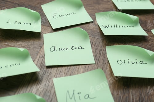 Preview: Paper stickers with different names on wooden table, closeup. Choosing baby's name
