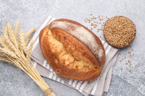 Preview: Loaf of sourdough bread, spikes and grain on grey table, flat lay