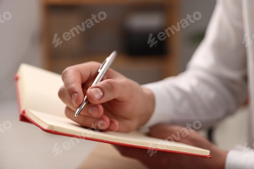 Preview: Man writing in notebook with pen indoors, closeup