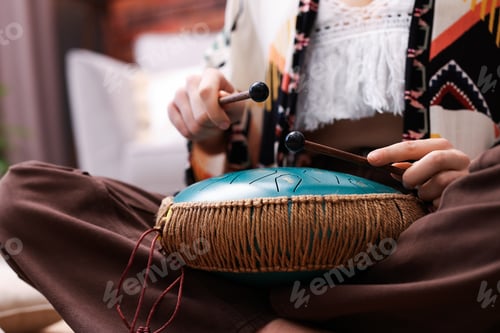 Preview: Woman playing steel tongue drum with mallets at home, closeup