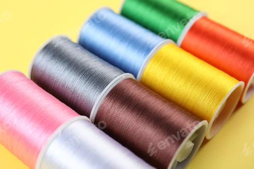 Preview: Spools of sewing threads on yellow background, closeup