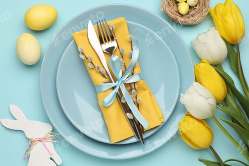 Preview: Easter celebration. Festive table setting with cutlery, tulips and painted eggs on light blue backgr