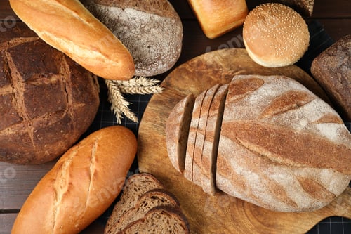 Preview: Different types of bread loaves and wheat spikes on wooden table, flat lay