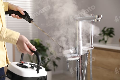 Preview: Woman cleaning faucet with steam cleaner in bathroom, closeup