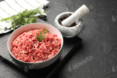 Preview: Raw minced beef meat with dill and peppercorns on black table, closeup. Space for text