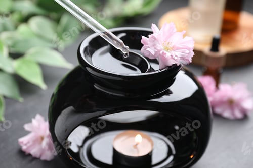 Preview: Aromatherapy. Dripping essential oil into aroma lamp on black table, closeup