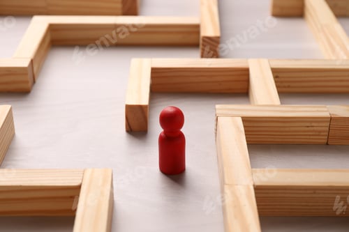 Preview: Maze made of wooden blocks and human figure on table, closeup. Business strategy