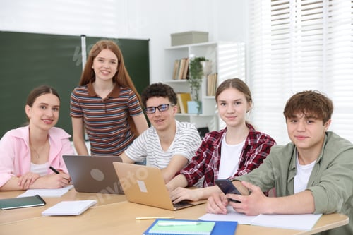Preview: Group of students studying with laptops and notebooks at wooden desk in classroom
