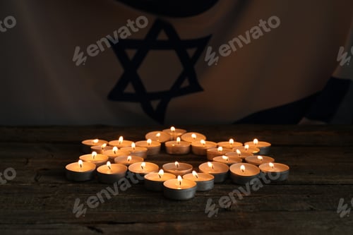 Preview: Holocaust Remembrance Day. Burning candles in shape of Star of David on wooden table against flag of