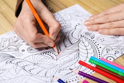 Preview: Woman coloring antistress picture with pencils at wooden table, closeup