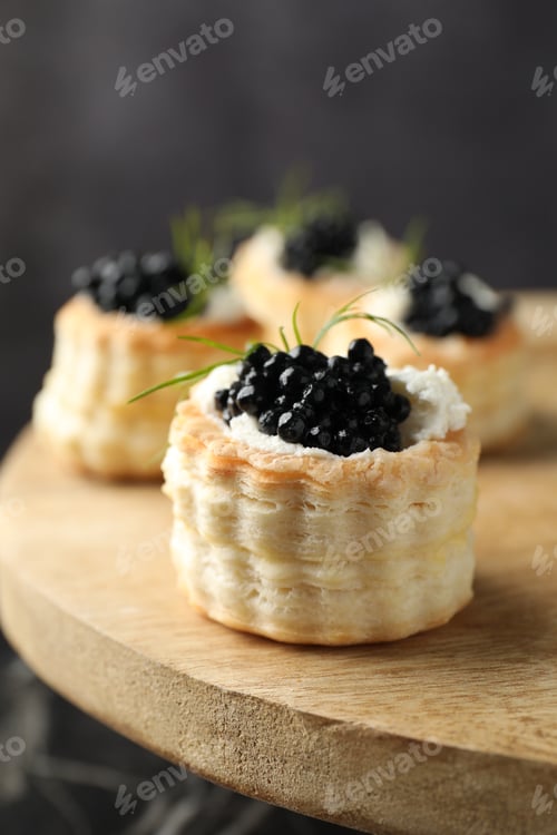 Preview: Tasty puff pastries with cream cheese, black caviar and dill on wooden stand, closeup