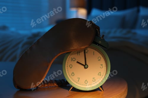 Preview: Alarm clock and sleeping mask on table in bedroom at night, closeup