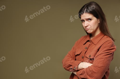 Vista previa: Portrait of resentful woman with crossed arms on dark green background. Space for text