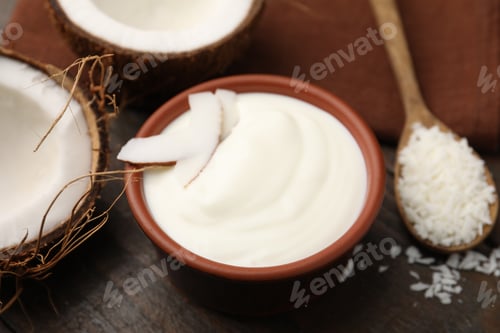 Preview: Delicious coconut yogurt in bowl, flakes and halves of fruit on wooden table, closeup