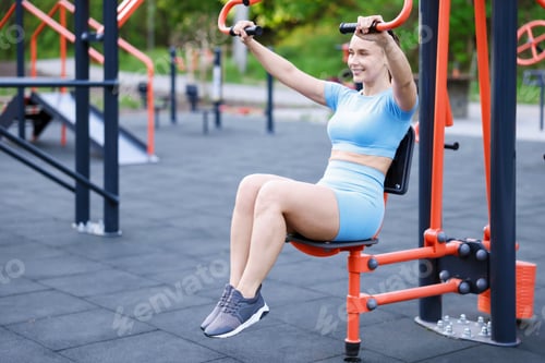 Preview: Athletic woman exercising on chest press machine at outdoor gym. Space for text