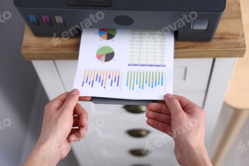 Preview: Man taking printed sheet of paper from printer at chest of drawers, above view