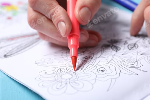 Preview: Woman coloring antistress picture with felt tip pen at light blue wooden table, closeup