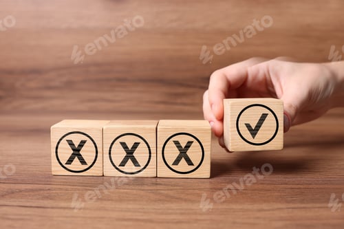 Preview: Woman putting cube with checkmark next to others with cross marks on wooden table, closeup. Followin