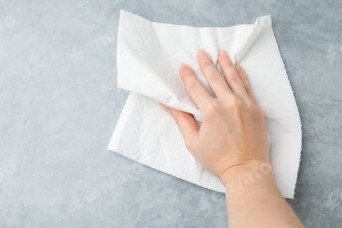 Vista previa: Woman wiping gray textured table with paper towel, top view. Space for text