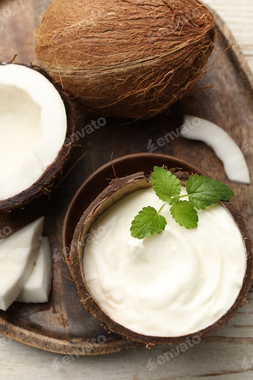 Preview: Tasty coconut yogurt with melissa leaves in shell and nuts on white wooden table, flat lay