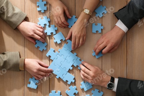 Preview: Team building. Group of businesspeople solving puzzle together at wooden table, top view