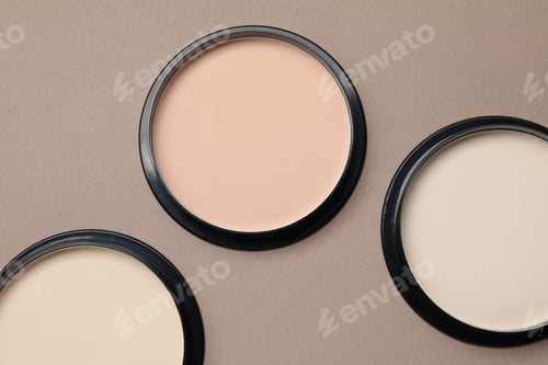 Vista previa: Face powder of different shades in containers on beige background, flat lay