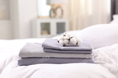 Preview: Stack of fresh linens and cotton flowers on bed indoors, closeup