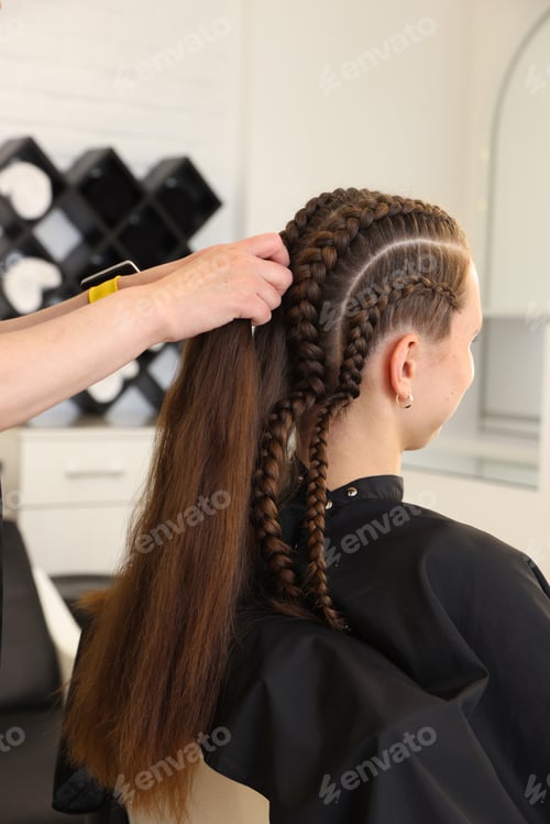 Preview: Hairstylist braiding teenage girl's hair in salon, closeup
