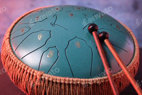 Preview: Steel tongue drum and mallets in red light on dark table, closeup