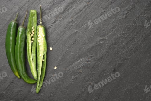 Preview: Fresh chili peppers on black textured table, flat lay. Space for text