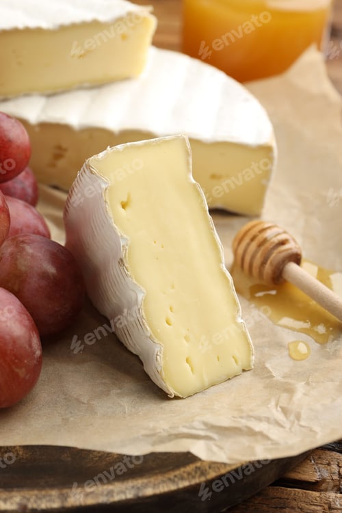 Preview: Slices of delicious brie cheese, grapes, honey and dipper on wooden table, closeup